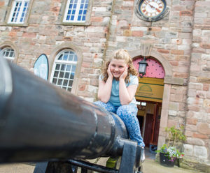 A girl sits on top of a canon in front of Berwick museum.