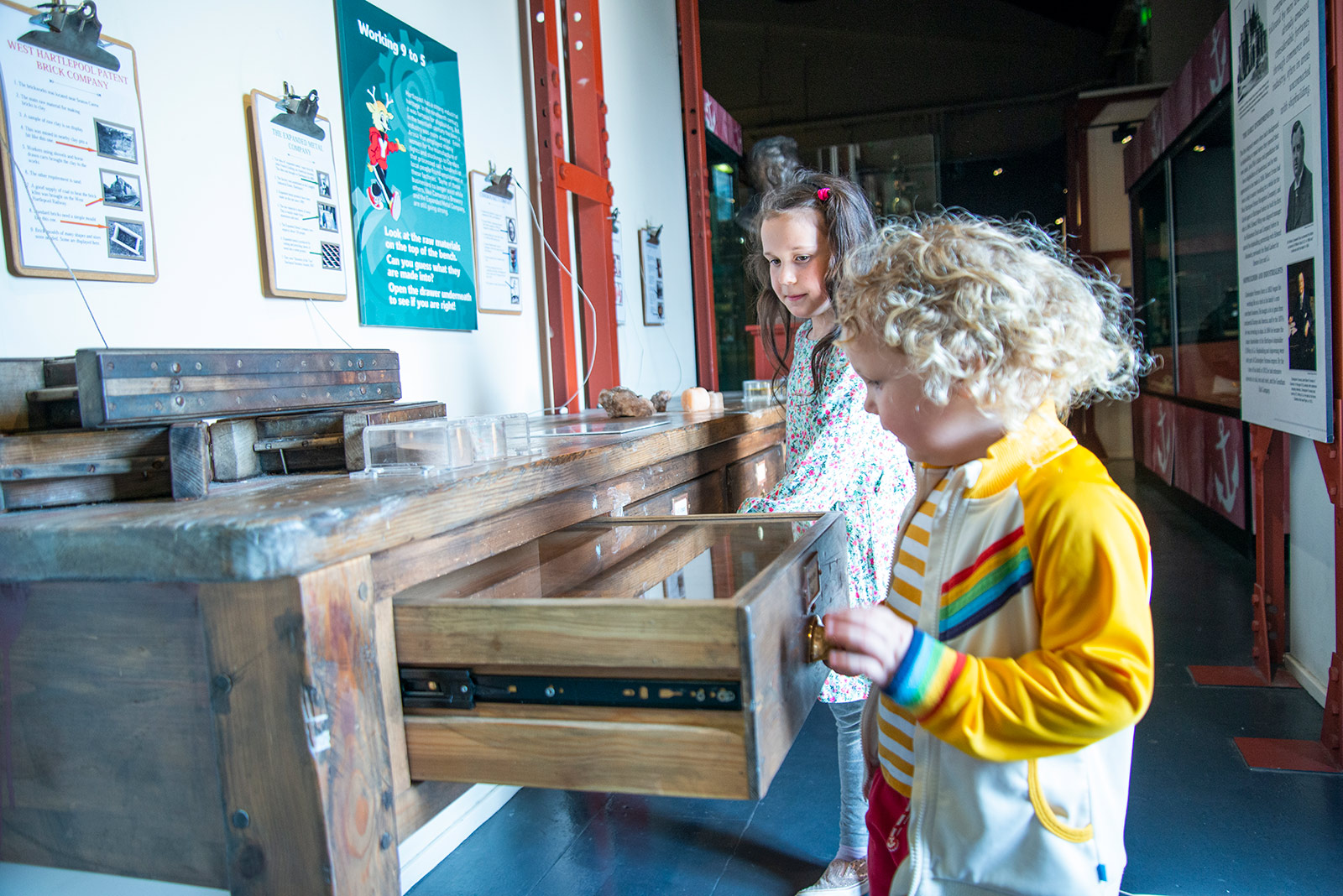 Two young girls explore drawers in a museum.
