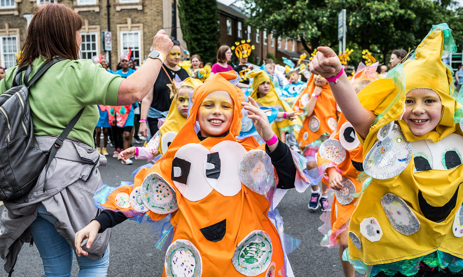 An image of a street parade with children dressed up as orange and yellow stars.