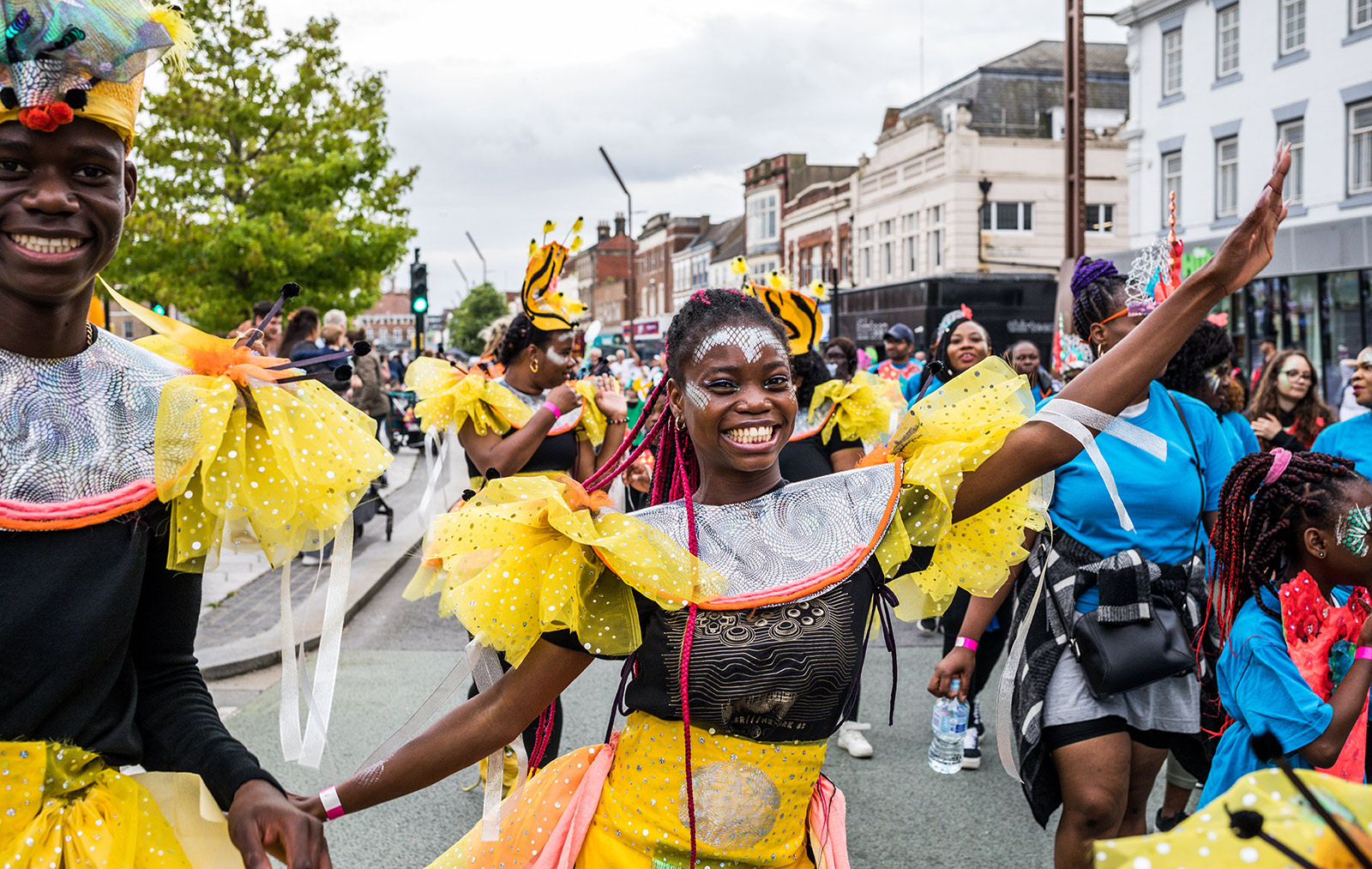 An image of a group of people taking part in a street parade through a town. They are dressed in bright yellow costumes with head pieces.