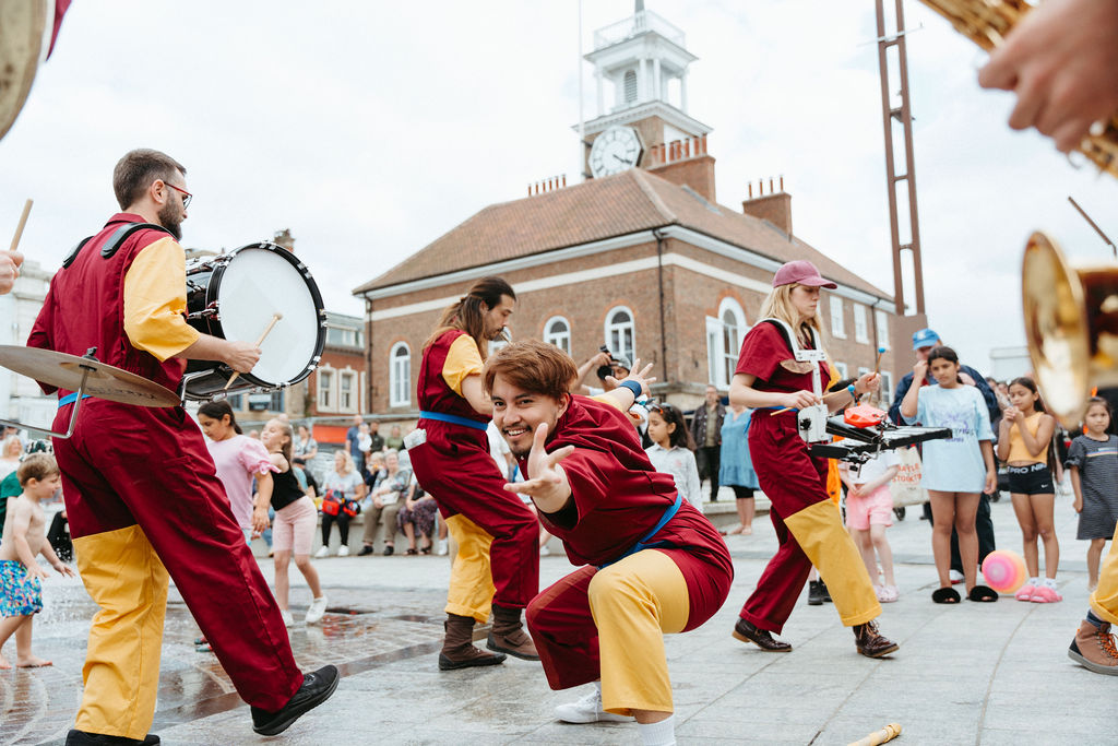 Street performers stand in a town square wearing and gold costume and playing musical instruments.