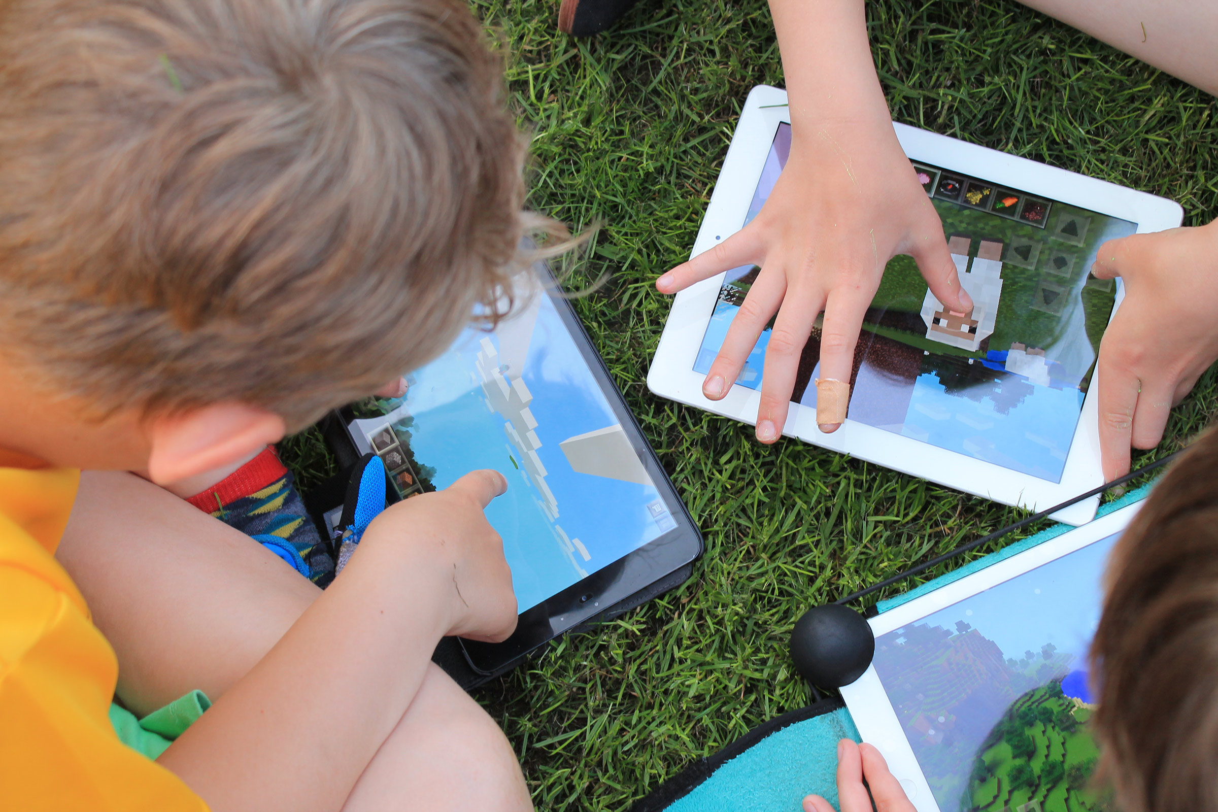 An image of children playing on iPads on grass. The image is taken from above looking down on them.