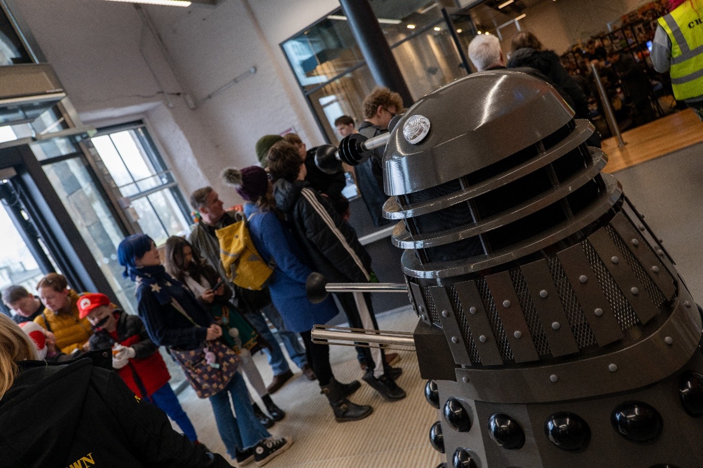 An image of a dalek in a room full of people.