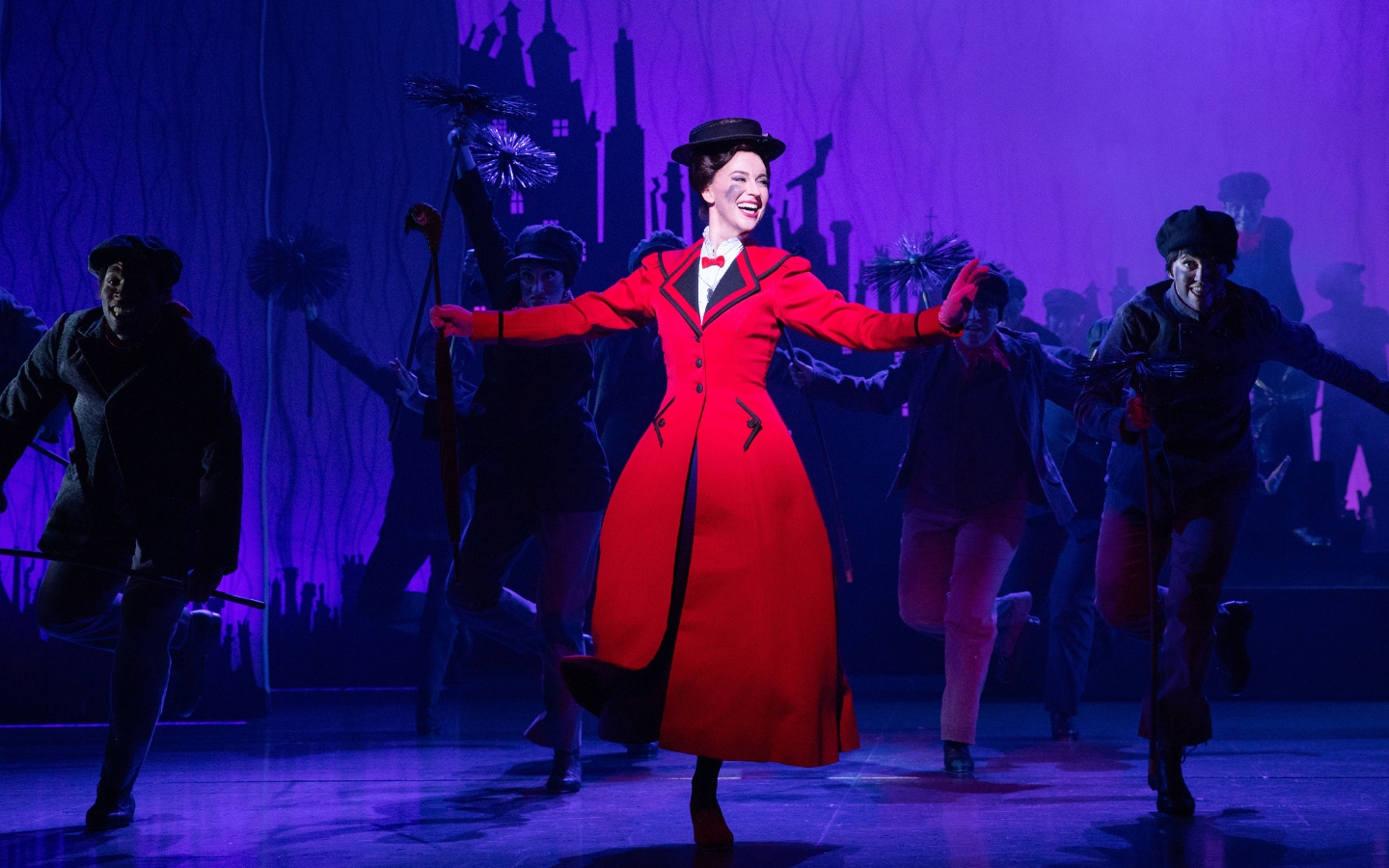 A woman in a bright red coat dances on a stage. She is Mary Poppins.