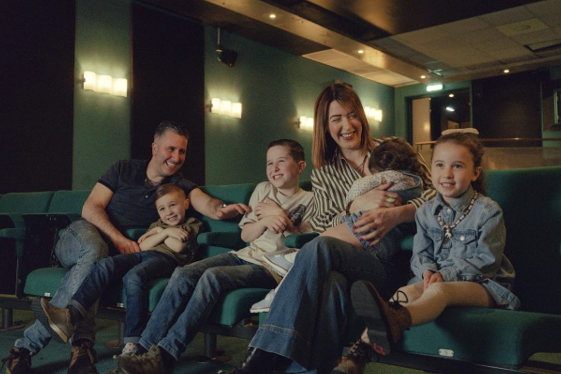 a family of 5 adults and two children are sitting in theatre seats, laughing.