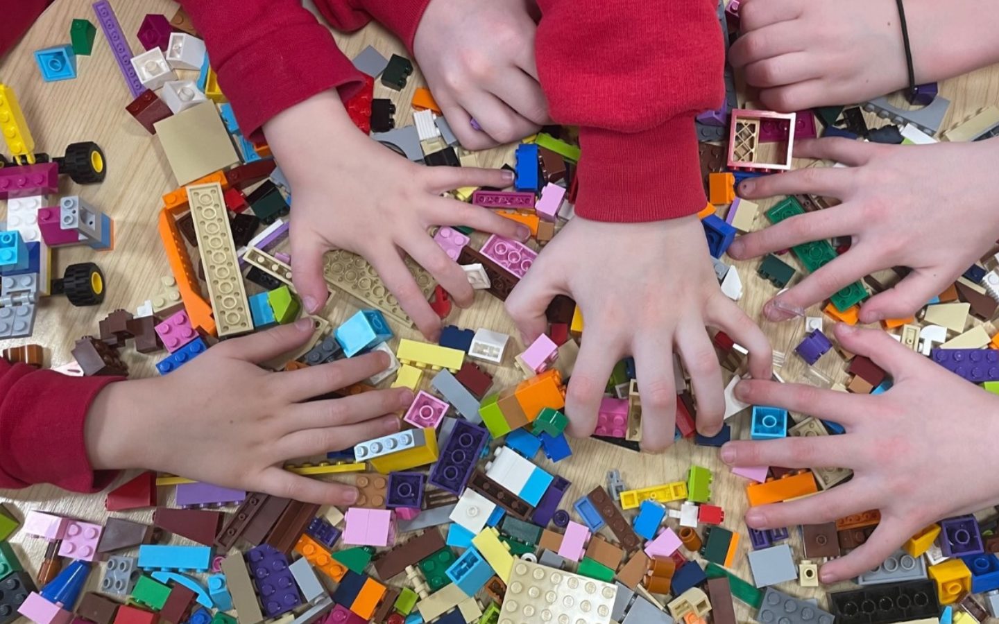 Three sets of children's hands rummage around a pile of Lego.