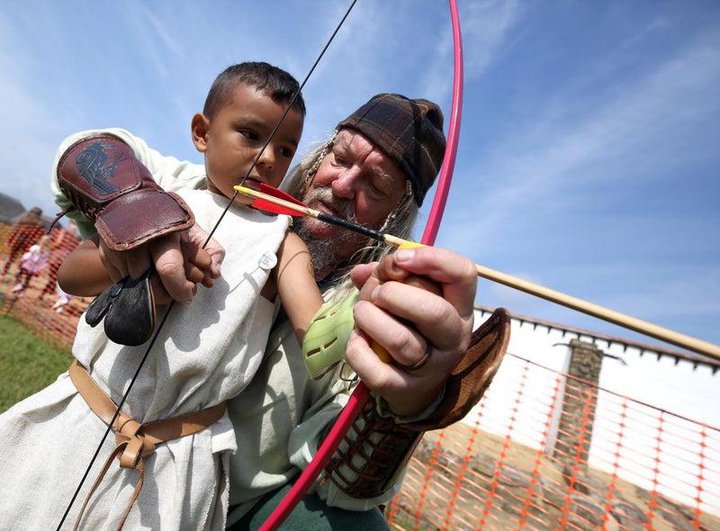 A man dressed as a gladiator holds a bow and arrow with a young boy.