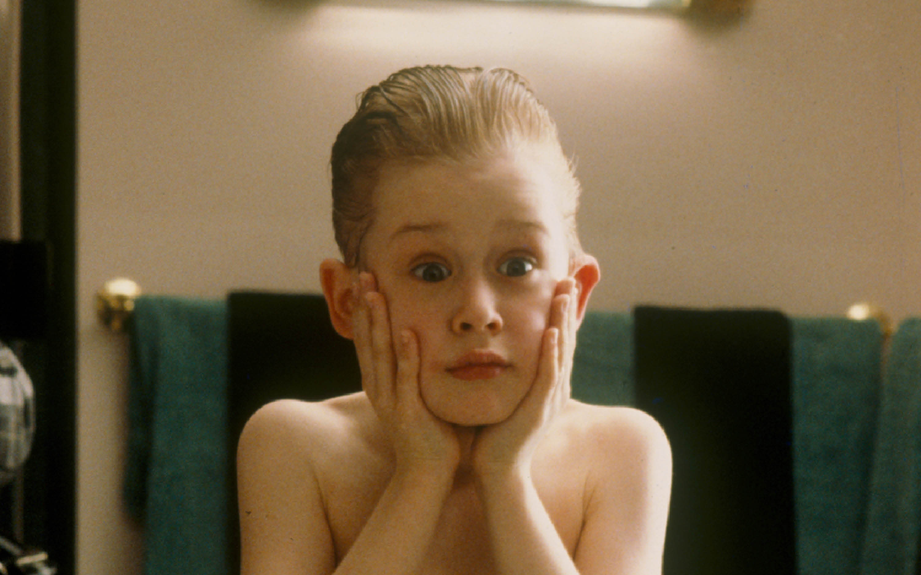 A child with greased back hair puts his hands on his face. He has a surprised expression.