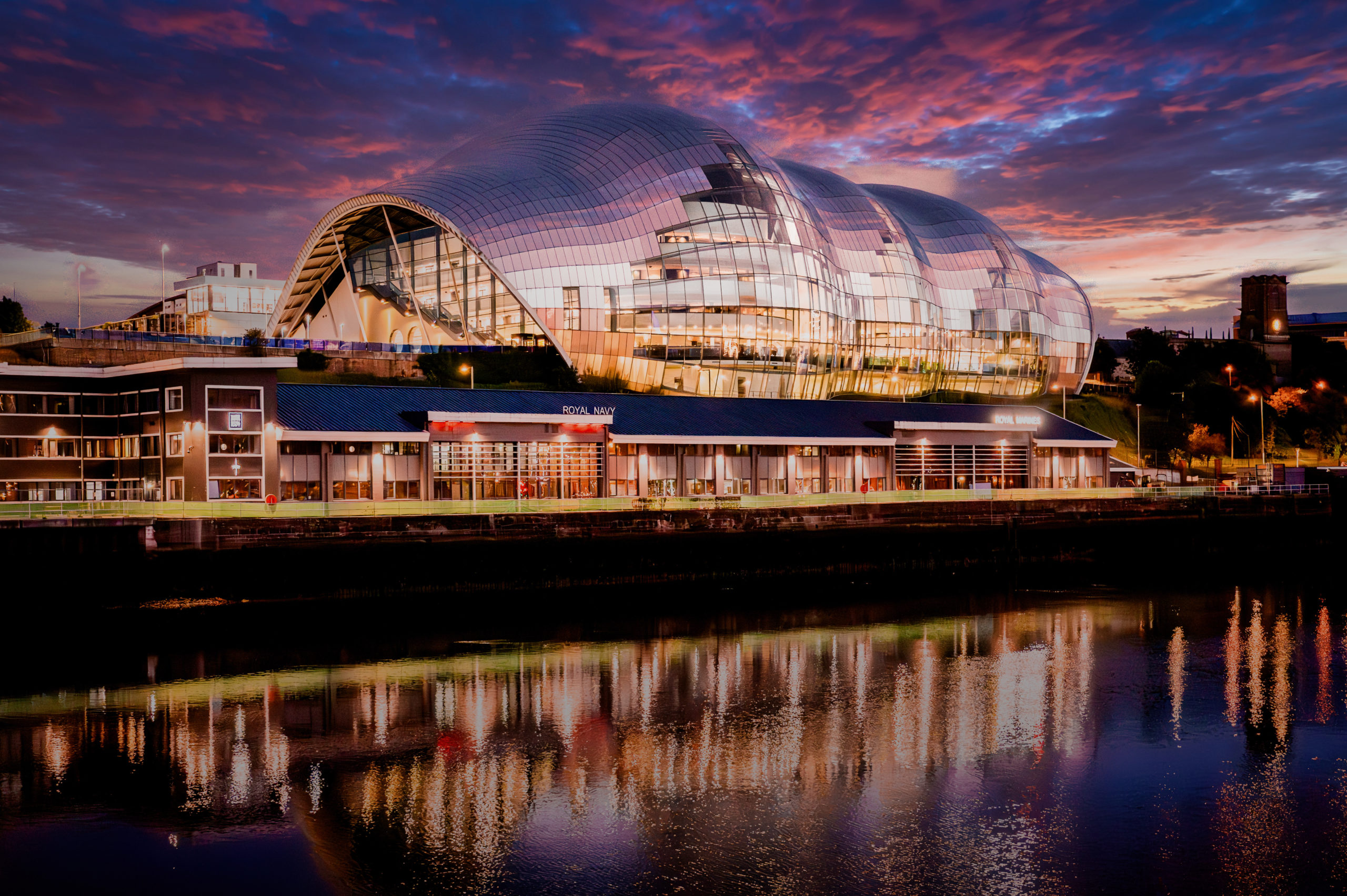The exterior of the Glasshouse, a glass building on the riverside with a curved, undulating silhouette.