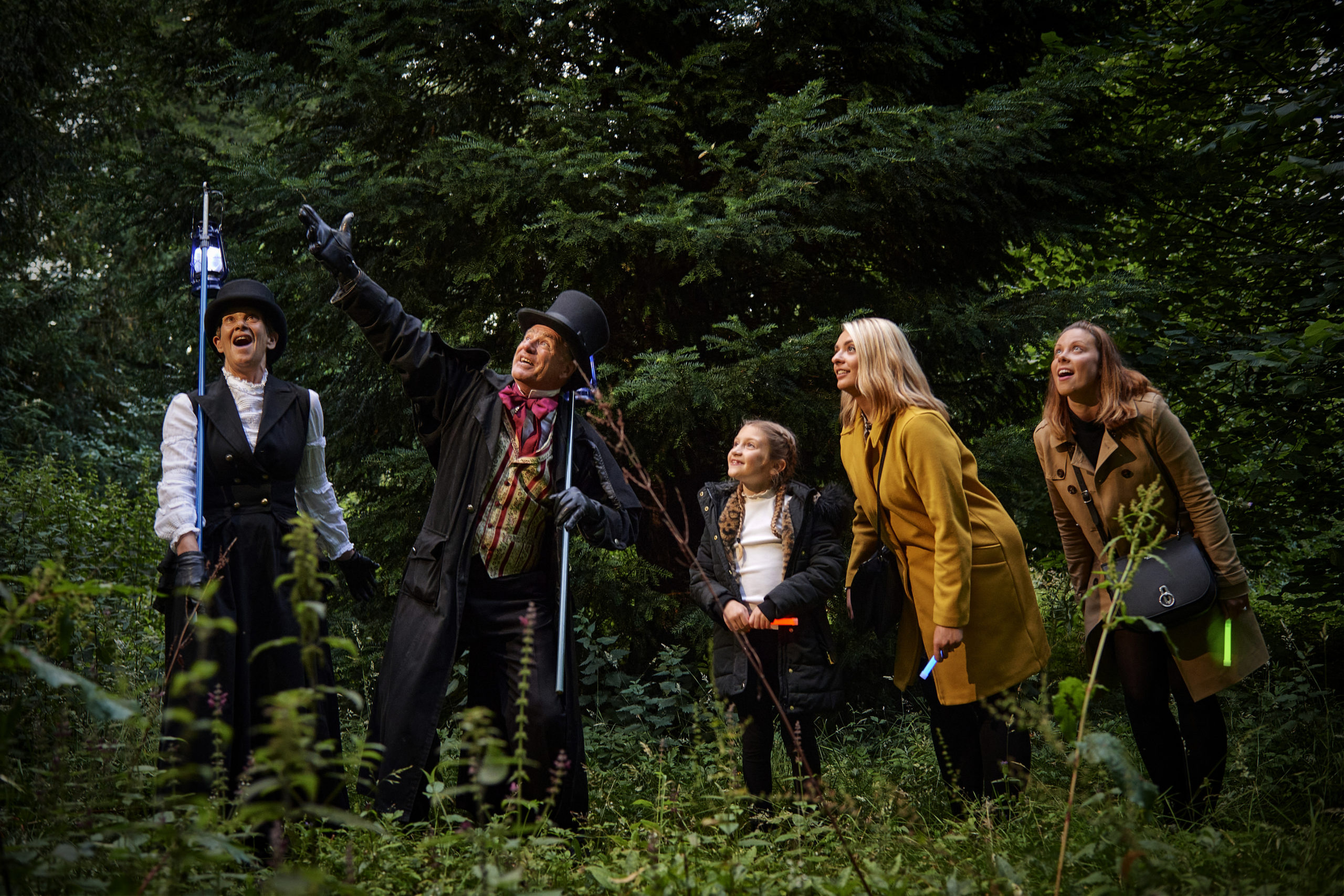 A group of people stand in woodland listening to two story tellers.