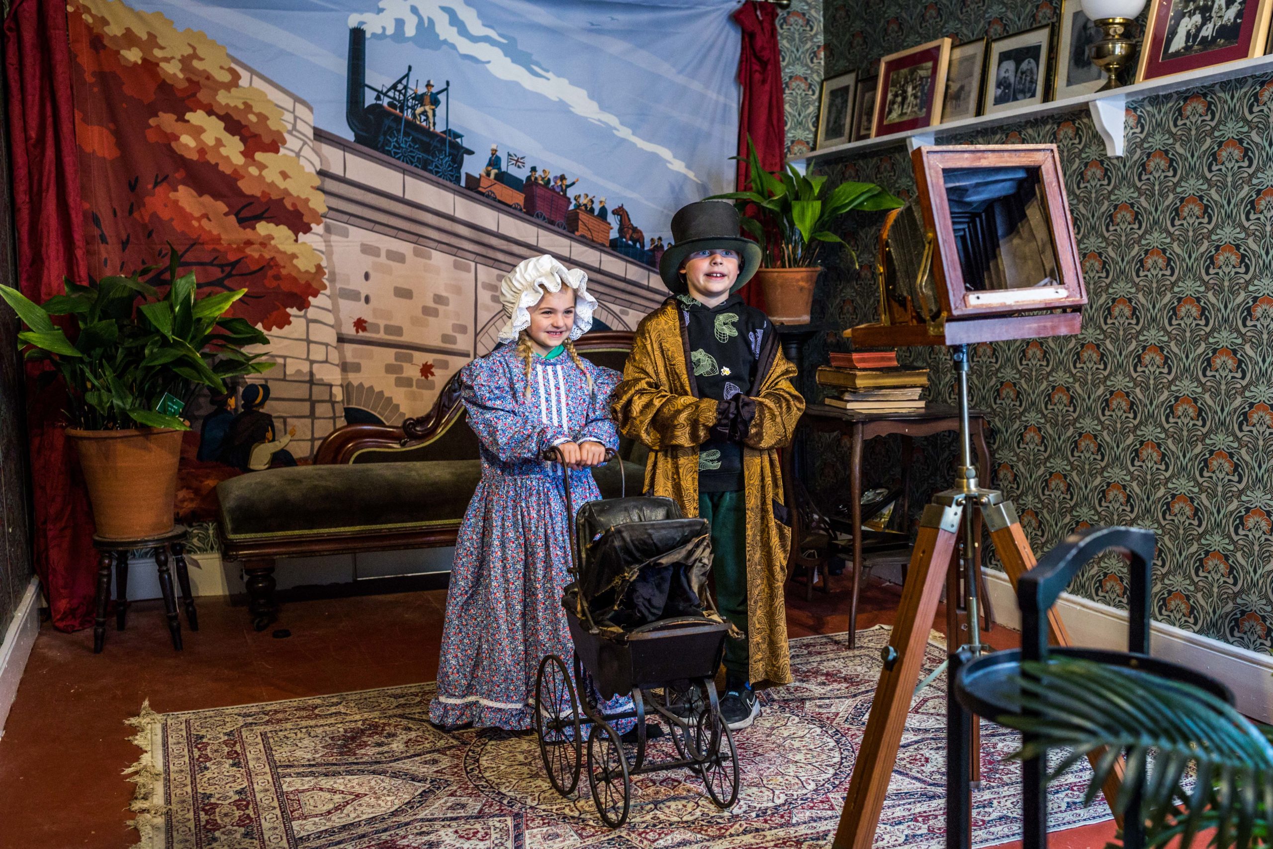 An image of a young boy and girl dressed in Victorian clothes in a room in a museum made to look like a Victorian house.