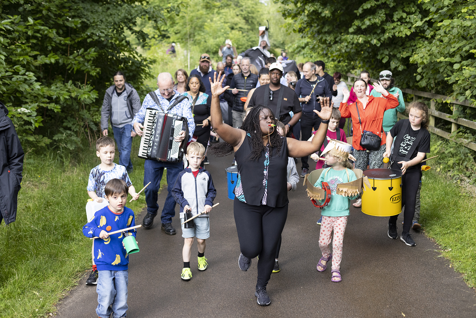 A large group of both adults and children parade through a forest.