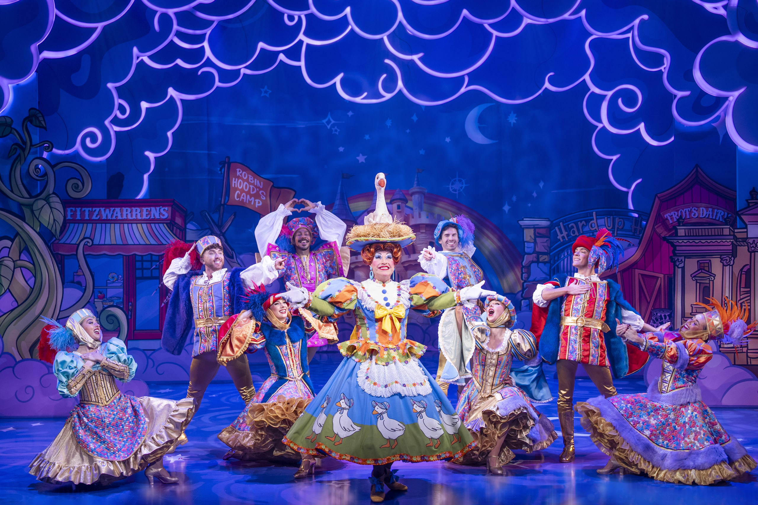 A group of performers are on stage in a pantomime with a pantomime dame in the middle.
