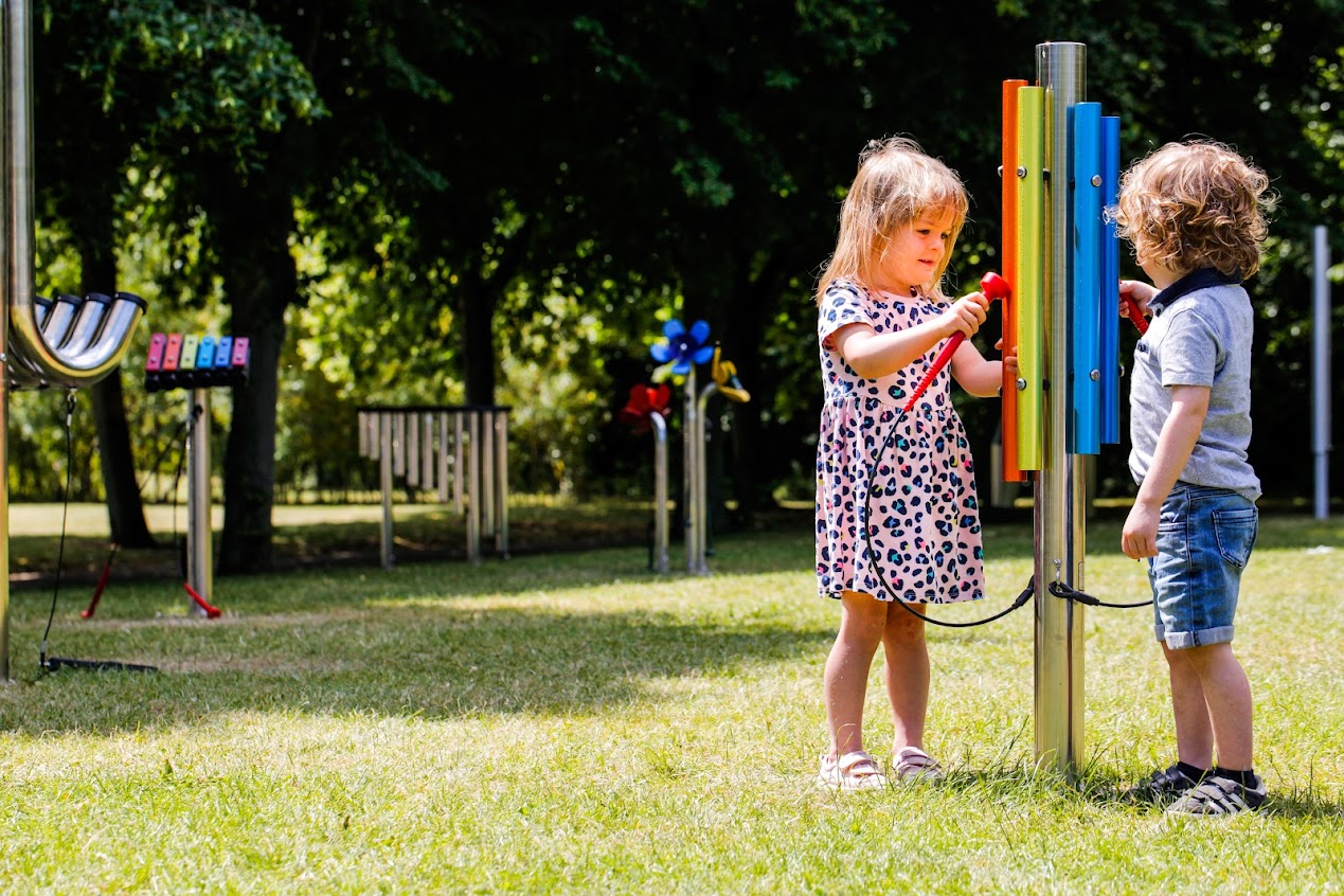 An image of two young children playing with outdoor musical instruments that are rainbow coloured in Kirkleatham Museum grounds.