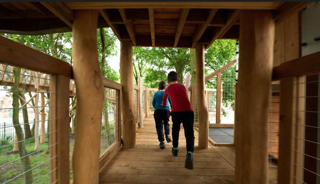 Two children run through a wooden tunnel in woodland.