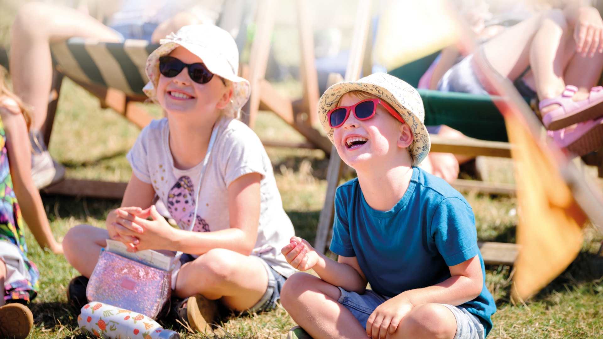 Two children sit on grass wearing sun hats and smiling.