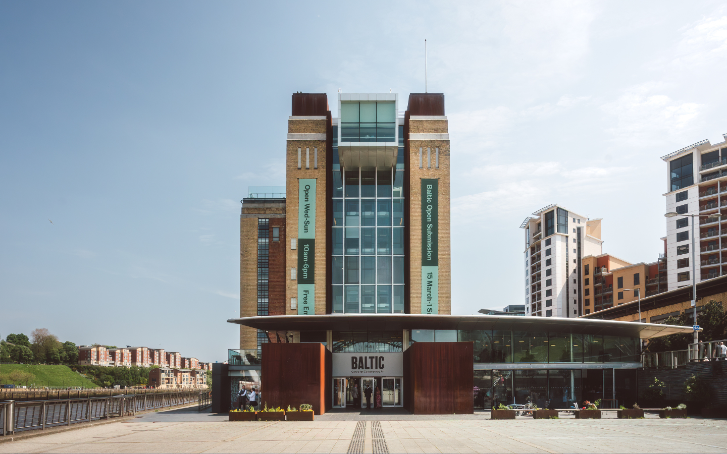 An image taken from the outside of the Baltic in Gateshead. It shows a seven storey brick building with a sign above the door that says Baltic.