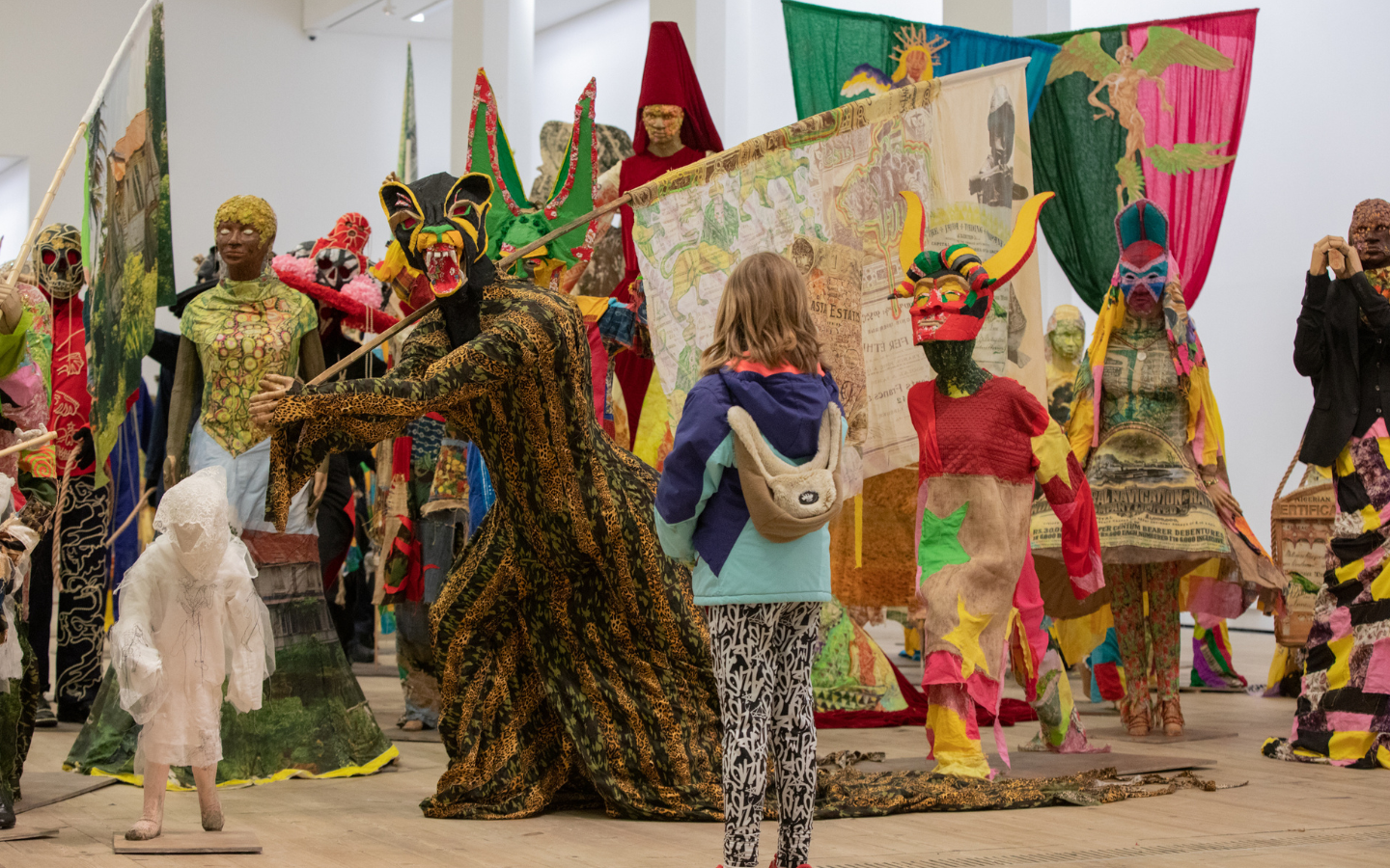 A room is filled with colourful flags, models and masks with a young girl stood with her back to the camera observing them.