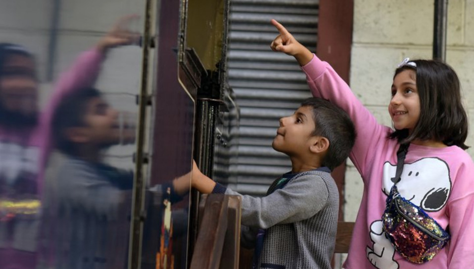 A young boy and young girl stand next to an old train carriage looking inside while the girls points at something up a height.