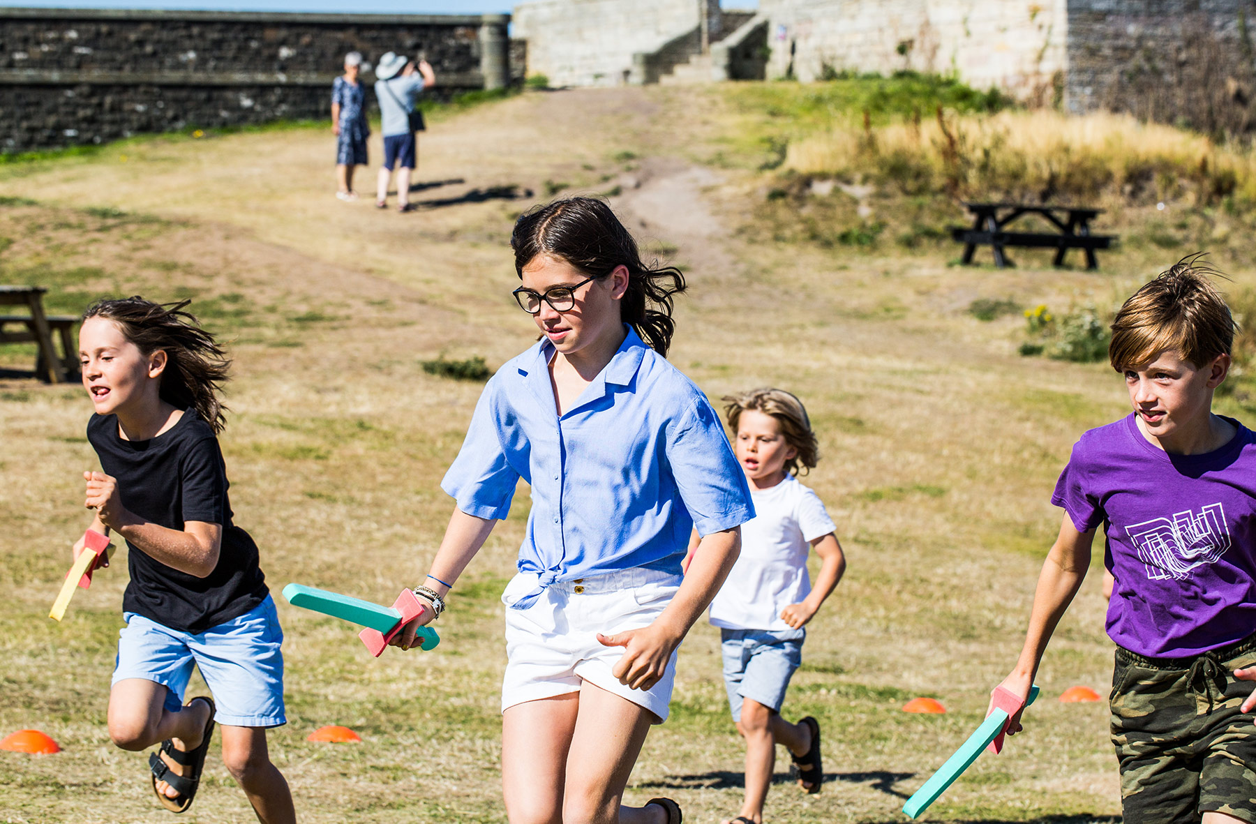 Children ranging in ages run outside holding blue foam swords.