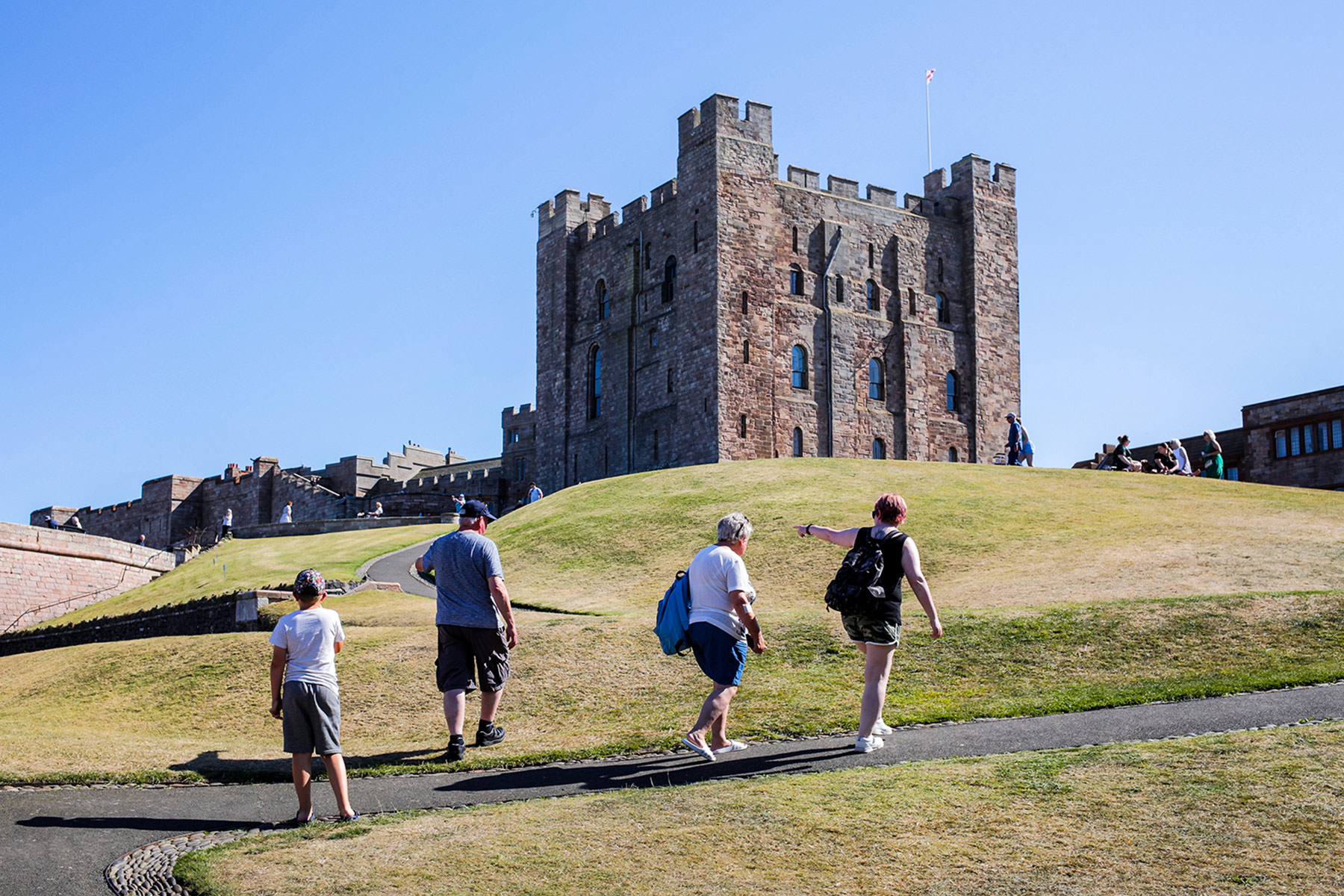 A group of four people walk along a footpath in front of a castle.