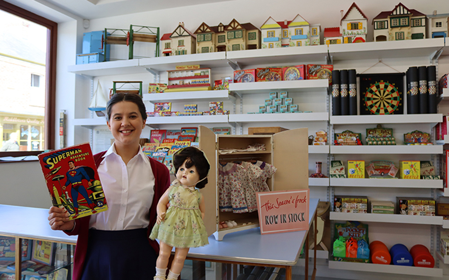 1950s Toy Shop at Beamish Museum A woman stands in a 1950s toy shop holding an old doll and a superman comic.