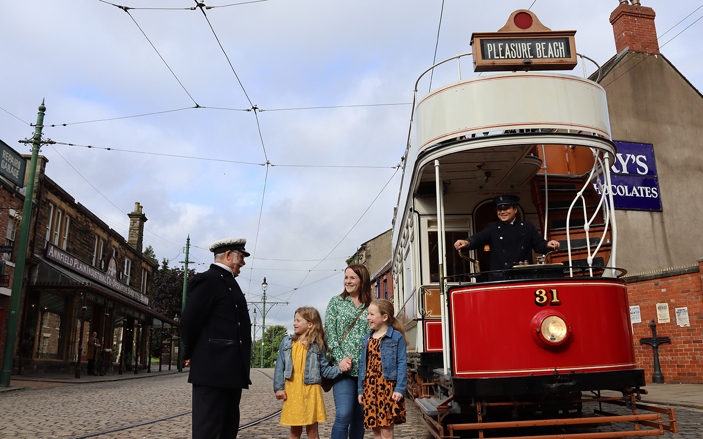 Beamish Museum, 1900s Town A tram conductor talks to a mother and two children as they stand next to an old tram with says Pleasure Beach on a sign on the top.