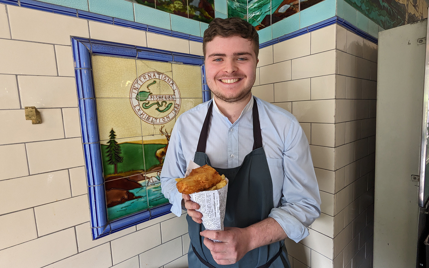 Davys Fish Shop at Beamish Museum A man stands in a fish and chip shop holding fish and chips wrapped in newspaper.