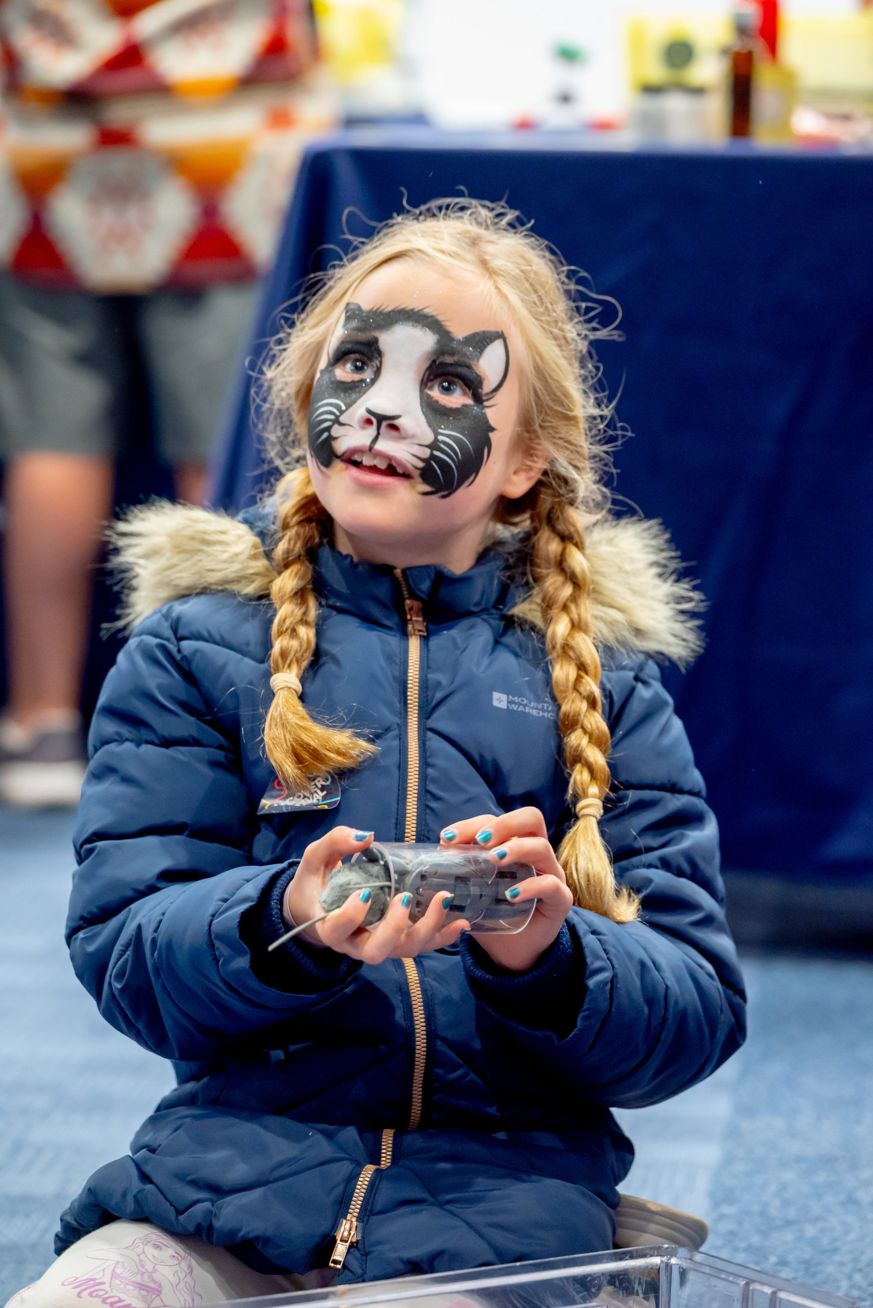 A child with their face painted as a cat holds an electronic object