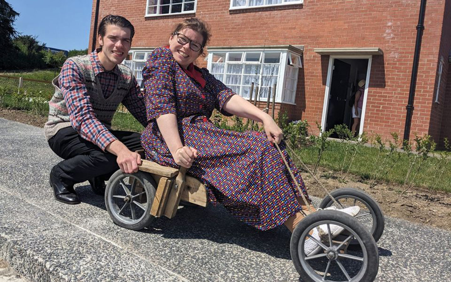 Explore new exhibits in The 1950s Town A man sits behind a woman on an old go-kart made from wood. They are in 1950s clothes.