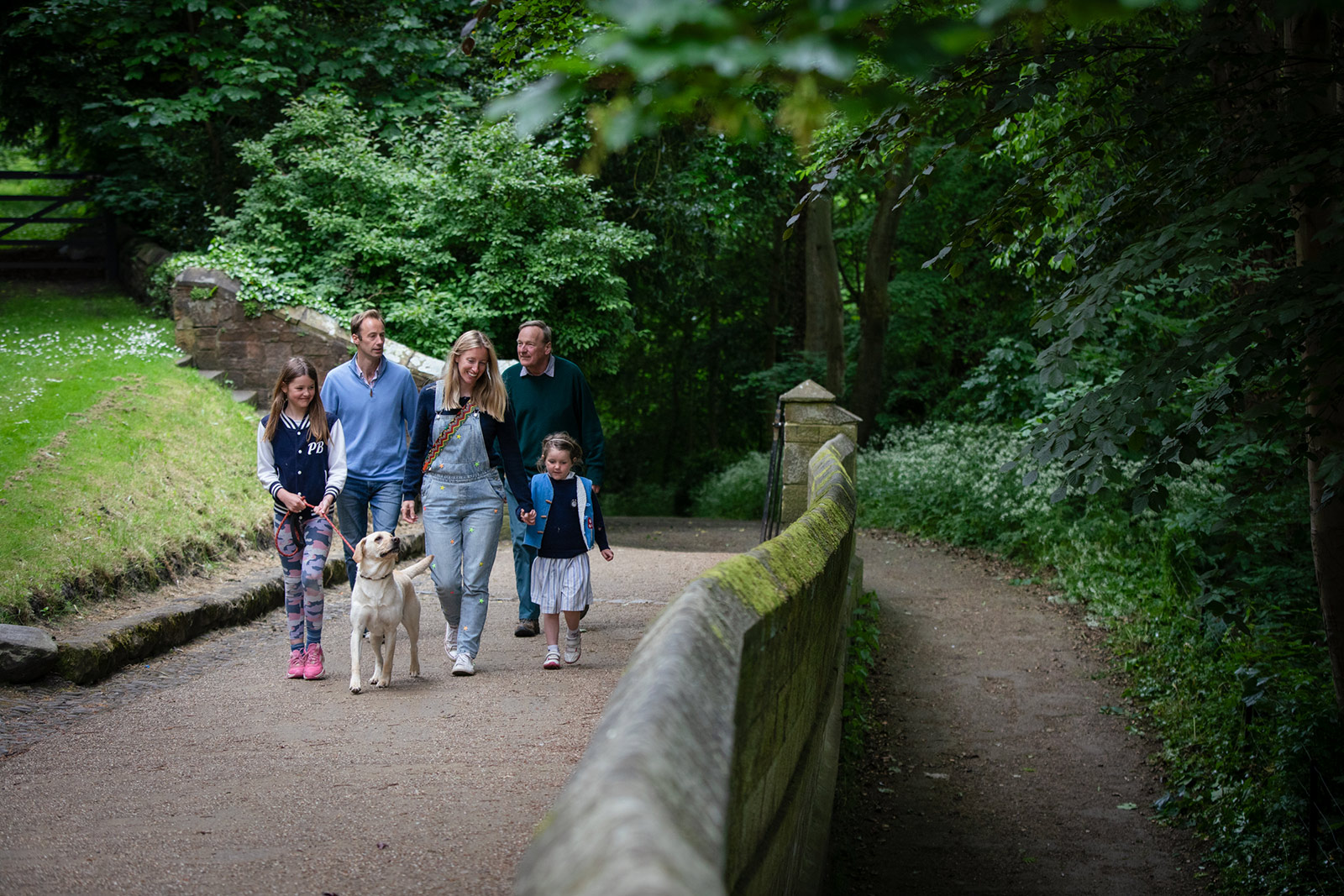 Family-dog-Riverbanks-015 A family group with a dog walk through a wooded area along a path beside a wall.