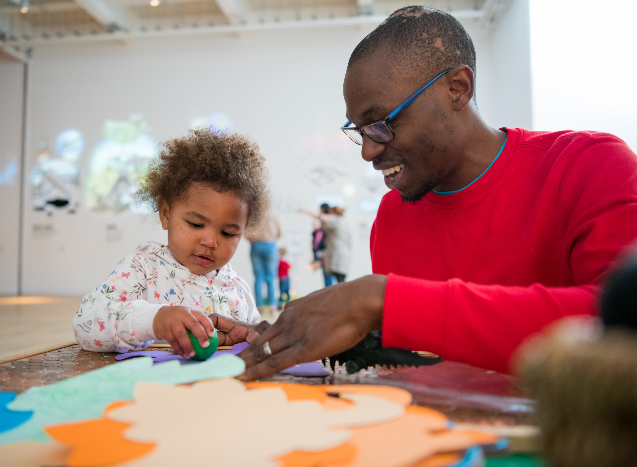 A father and toddler sit at a table doing crafts.