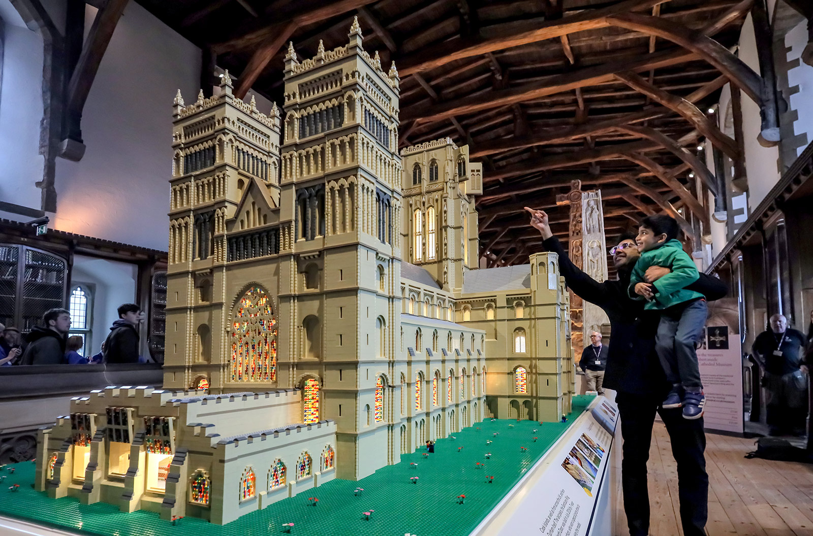 LEGO_DURHAM_CATHEDRAL_63 A man holds up a young boy as they look at Durham Cathedral made out of LEGO.