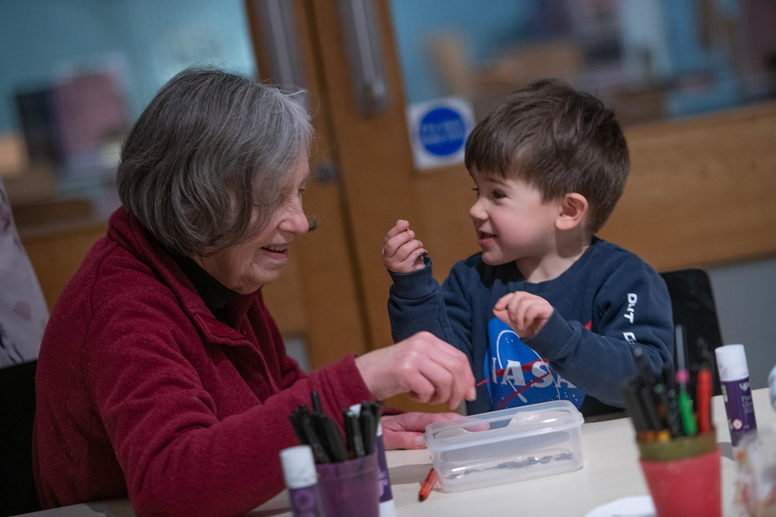 A young boy sits with his grandmother at a craft table.