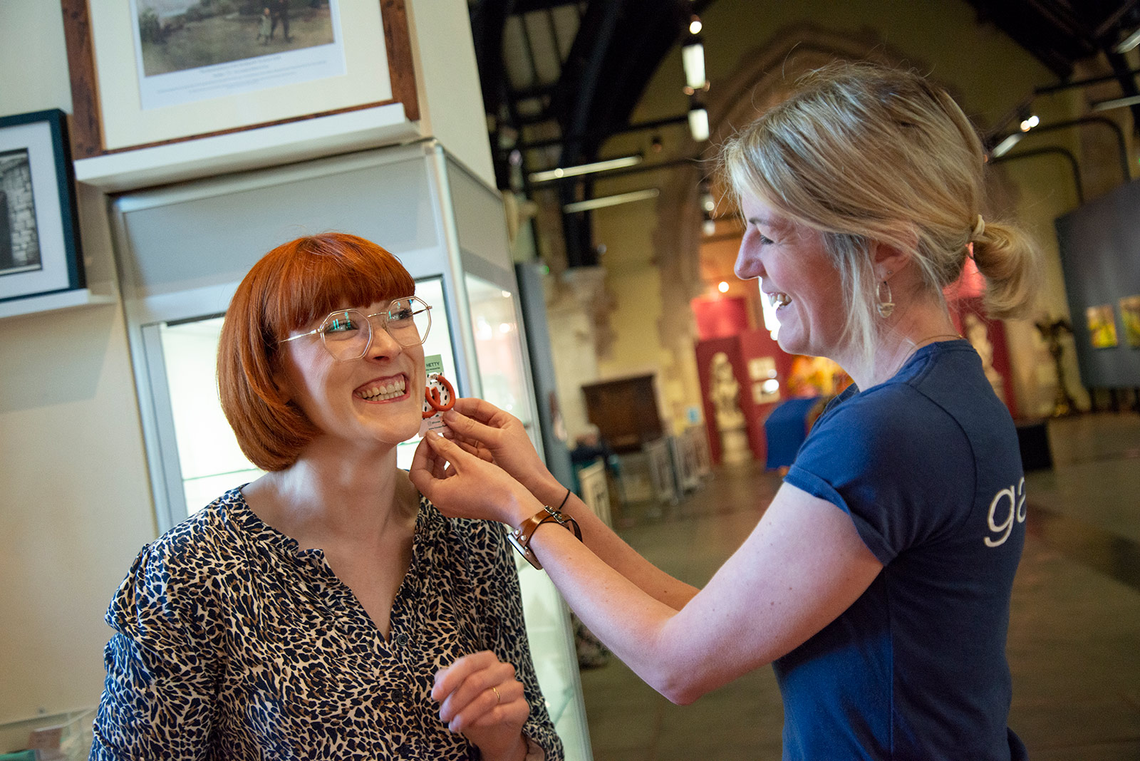 A woman is trying on earrings with another lady holding them up for her to try.