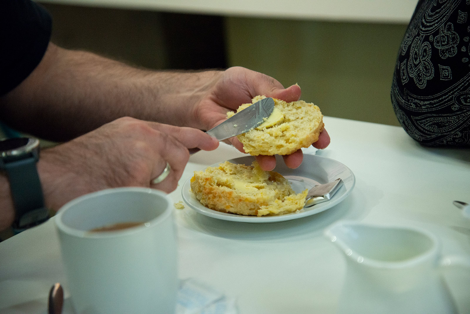 An image of a person spreading butter on a scone with a cup of tea beside the plate.