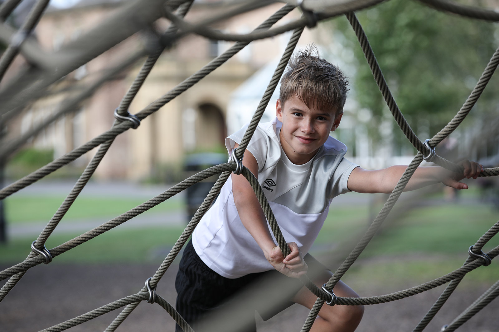 A young boy climbs in a play area web.