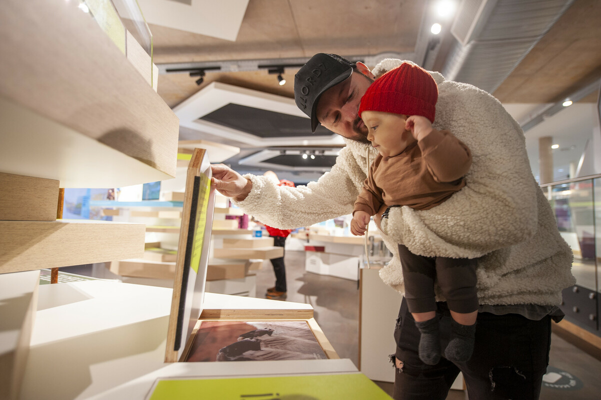 A man holds a baby as they look at a display in an exhibition.