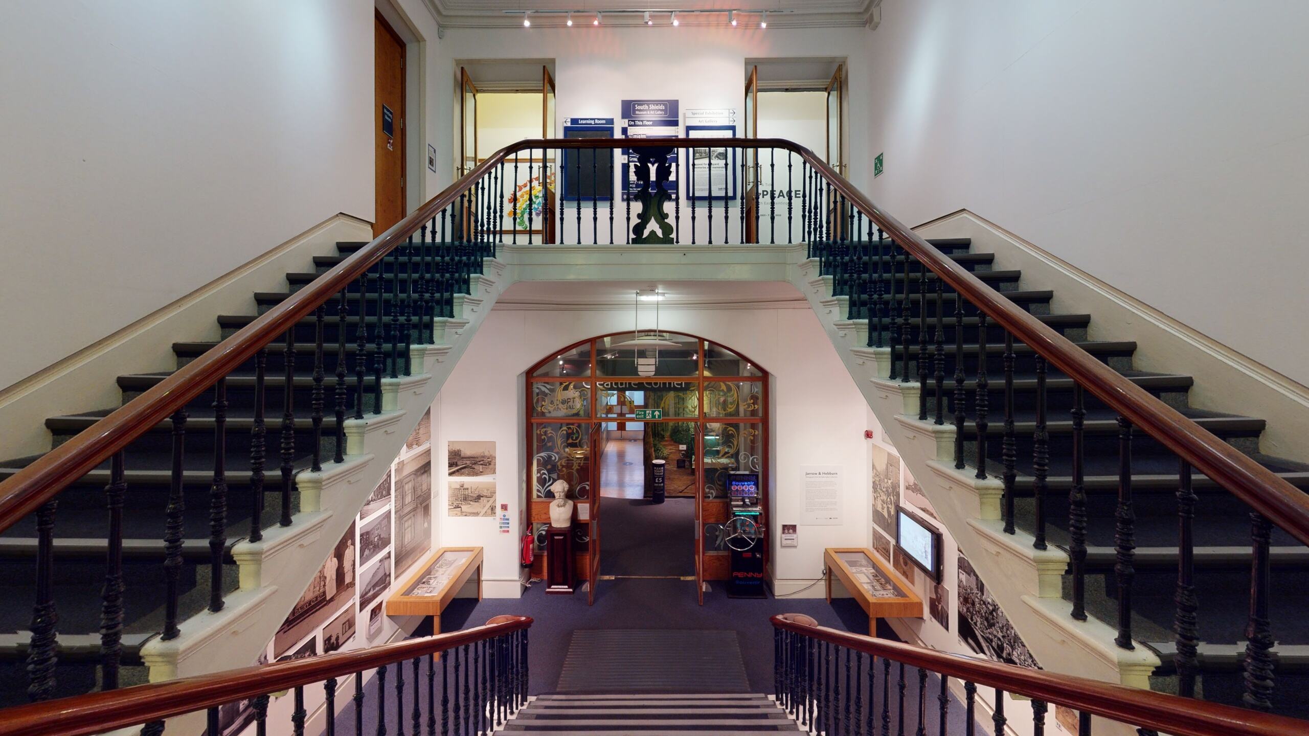An image of a grand staircase with banisters and stairs on the right and the left. There are also stairs leading down to a museum entrance.