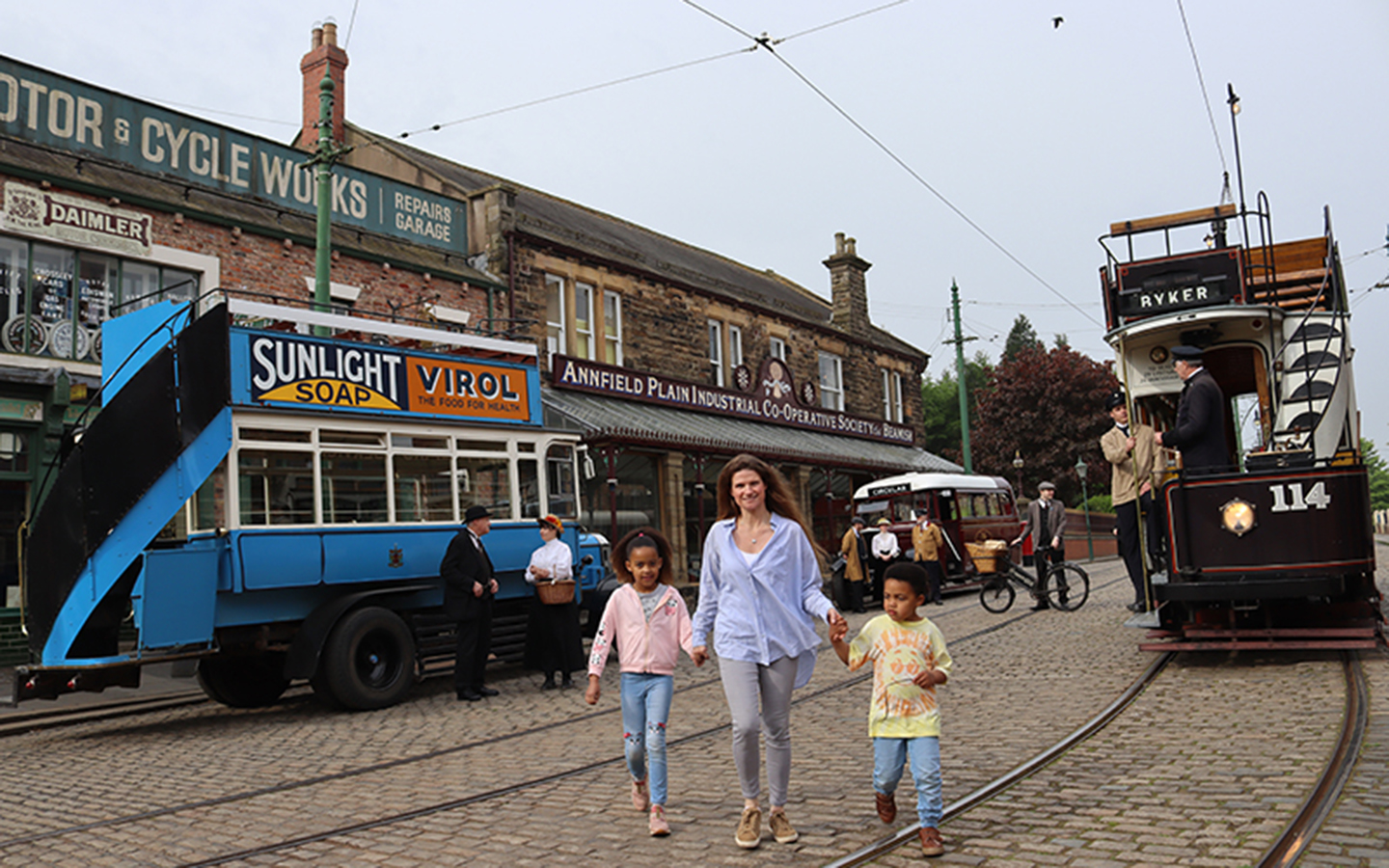 Take a trip back in time at Beamish, The Living Museum of the North A mother walks along a cobbled street holding hands with two young children. There are old trams and a pushbike in the background.
