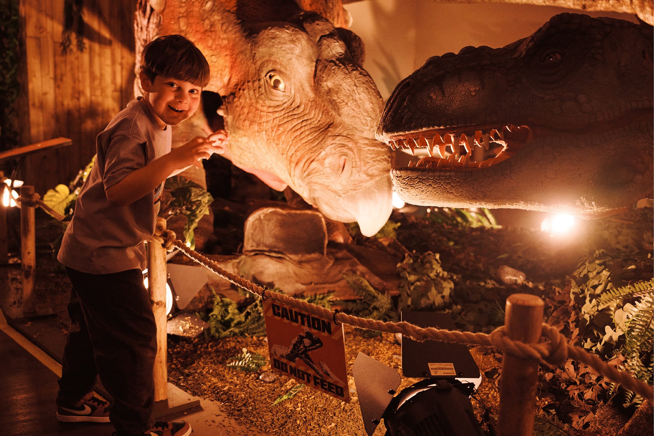 A child looks excited standing next to a huge dinosaur