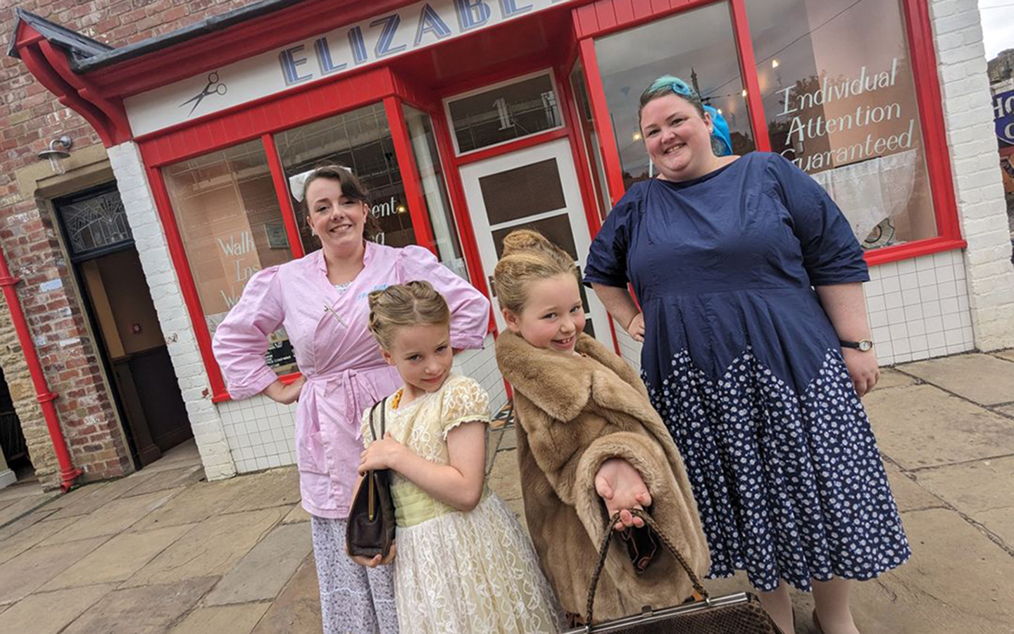 Visit the 1950s Hairdressers Two woman and two young girls are dressed in 1950s wear and standing in front of a 1950s hairdressers.
