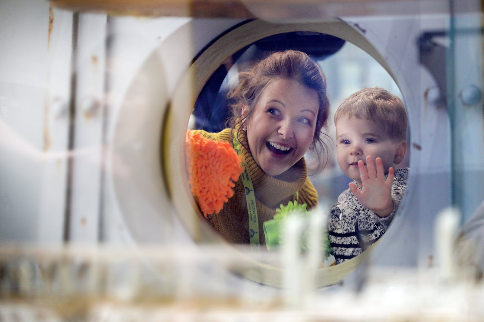 A mother and son look through a round glass window at a display in a museum.
