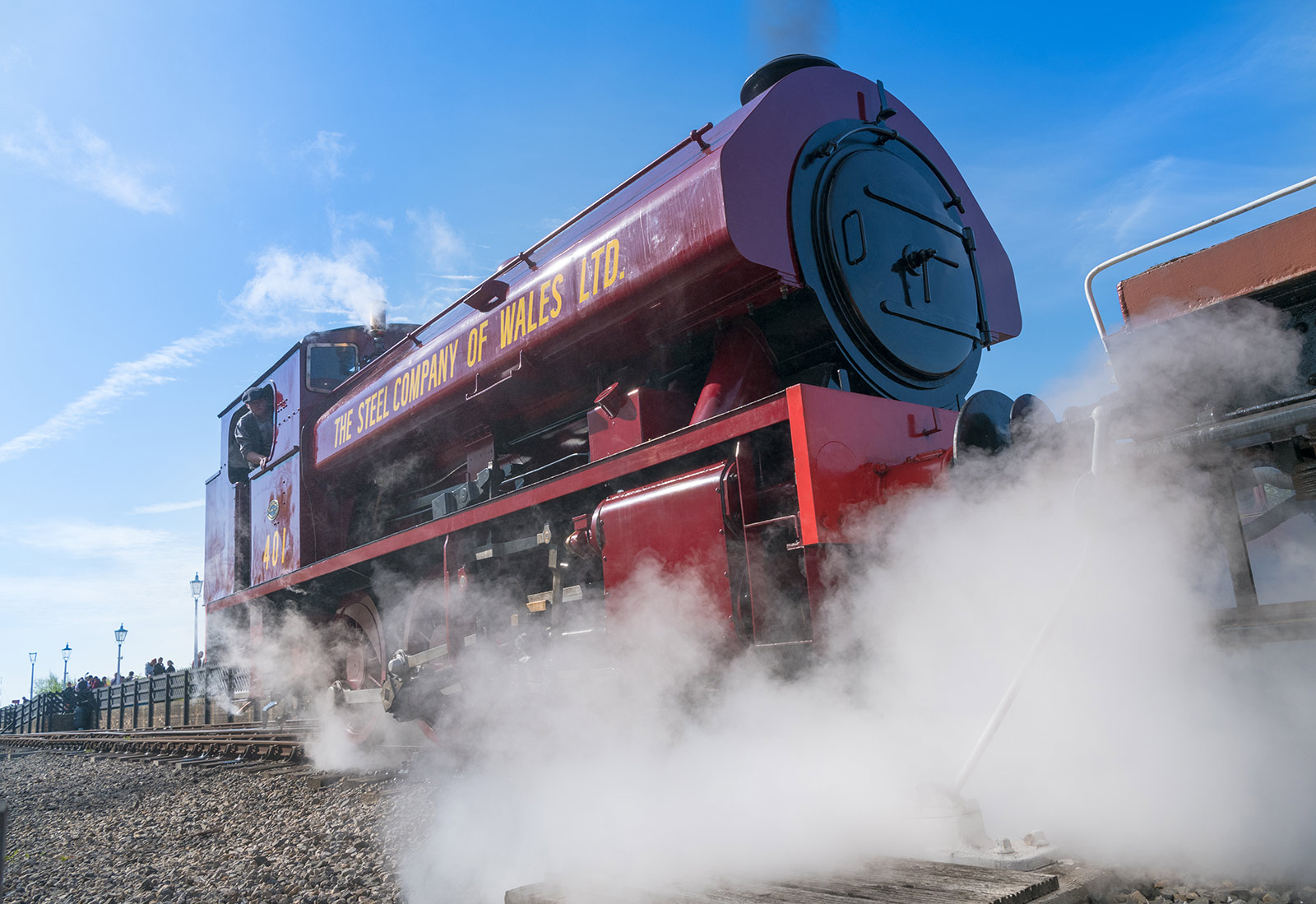 A large red steam engine puffs out steam as it sits on a railway line.