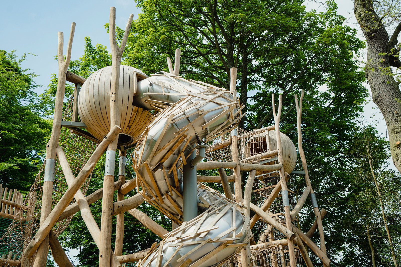 A naturally made playarea surrounded by trees. The structure is tall and includes a curly slide.