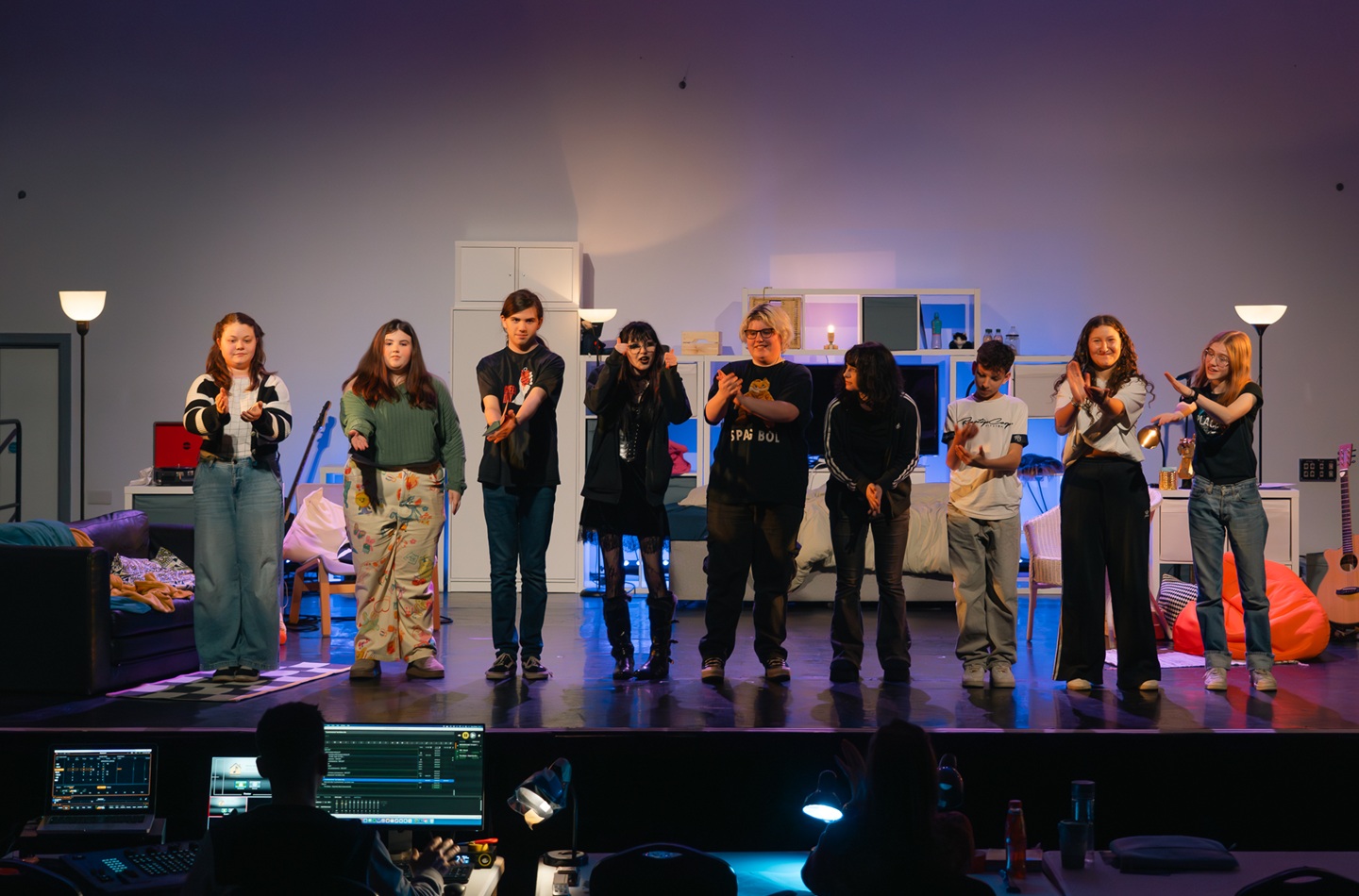 Nine young people stand in a row on a stage.
