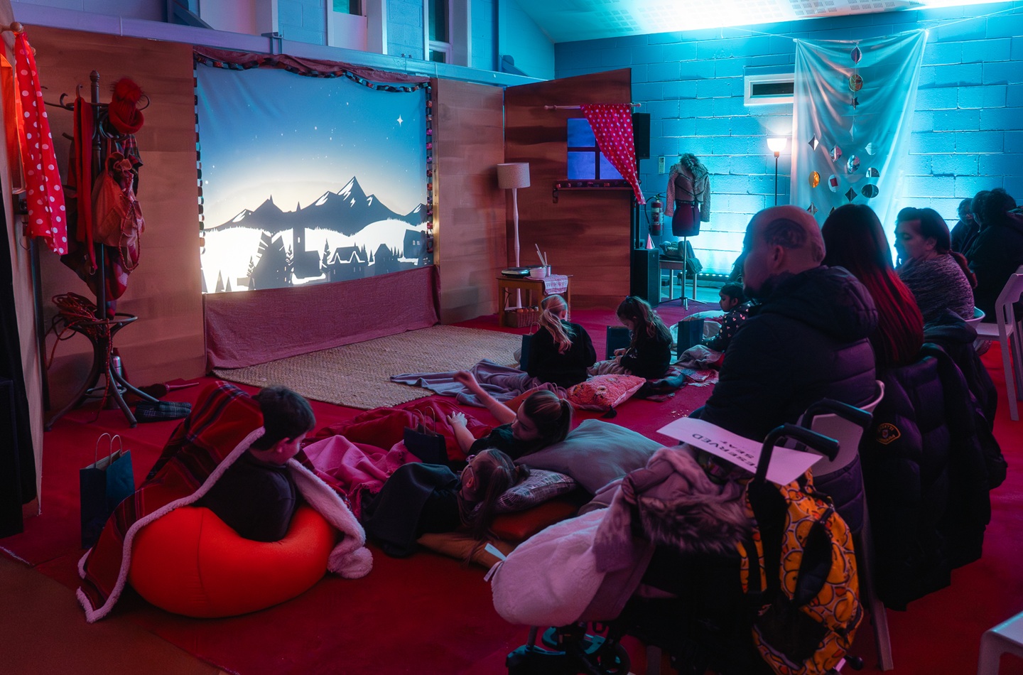 A group of people are seated watching a large screen in an ambiently lit red room.