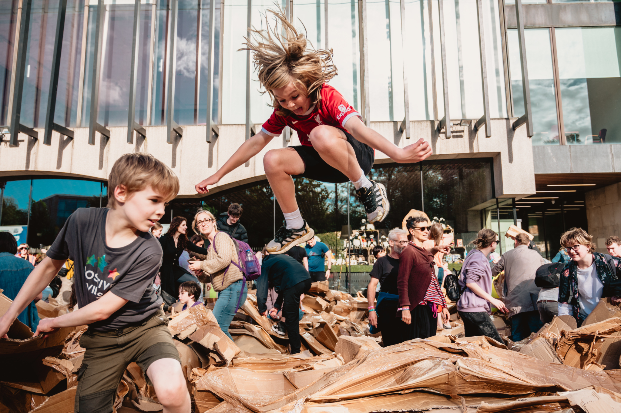 A child jumps high in the air, destrying a cardboard structure.