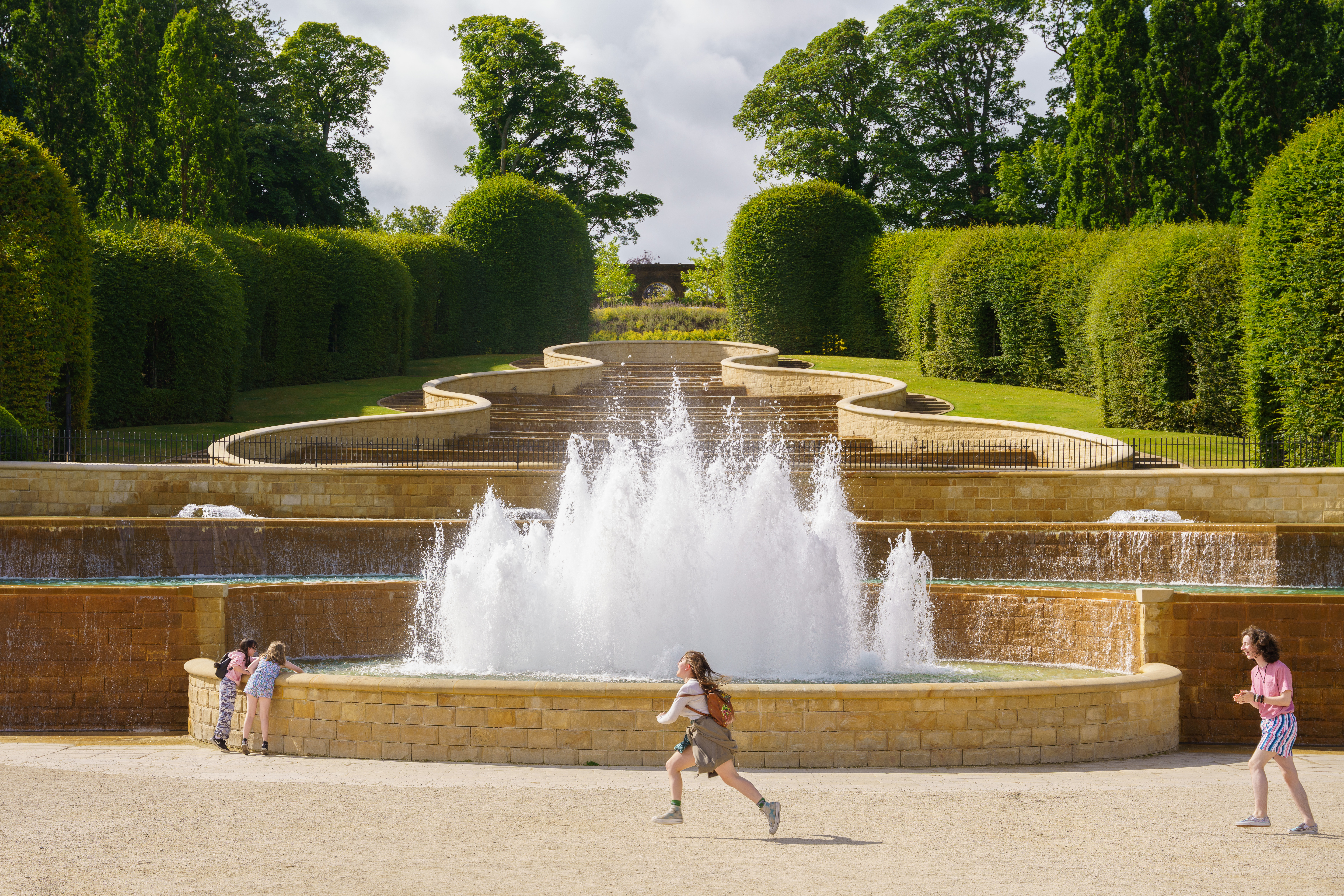 A child runs past a fountain with stepped tiers behind it.
