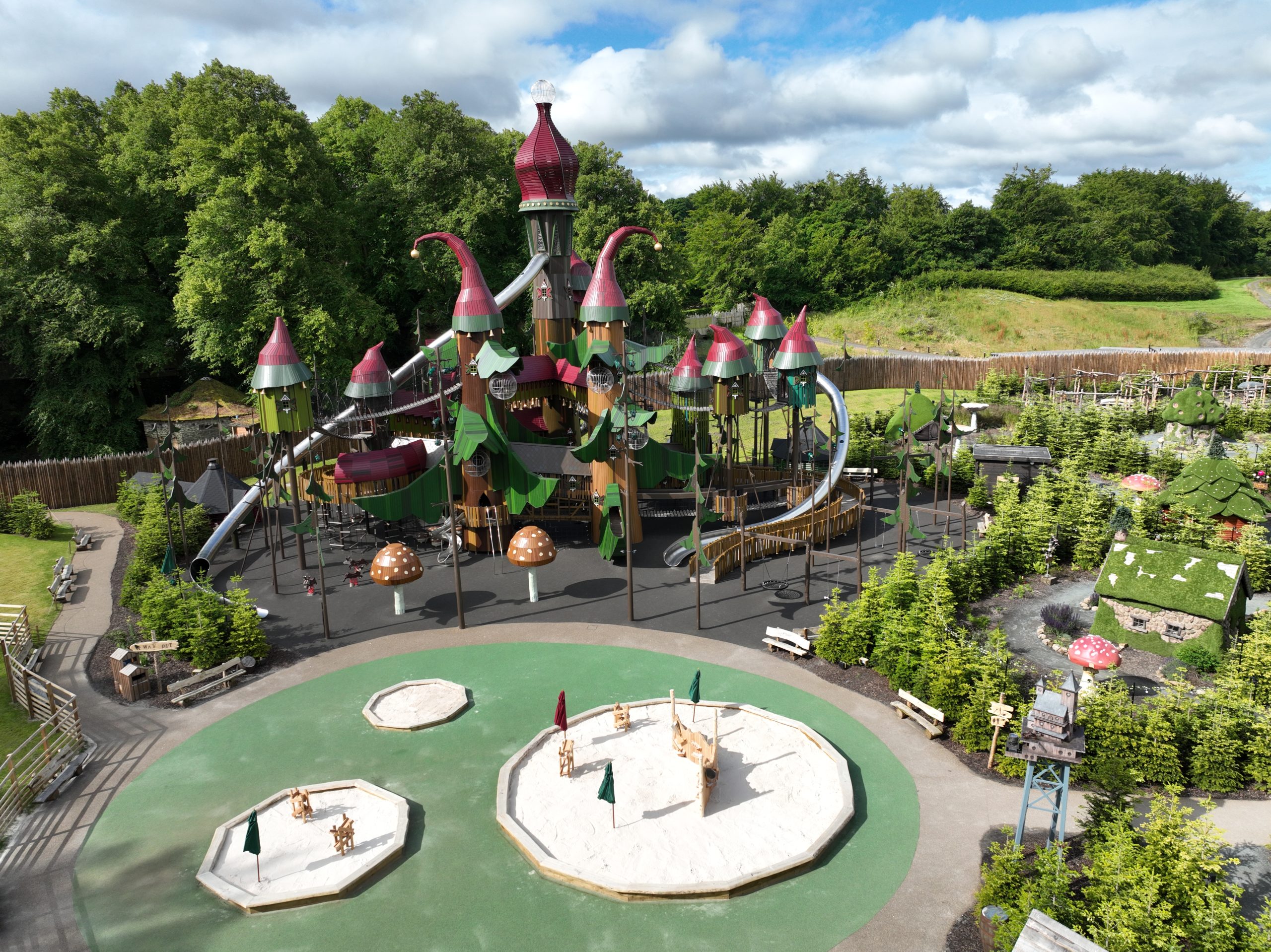 An ariel view of a large, colourful play area with woodland all around and large hexagonal platforms with small flags on them.